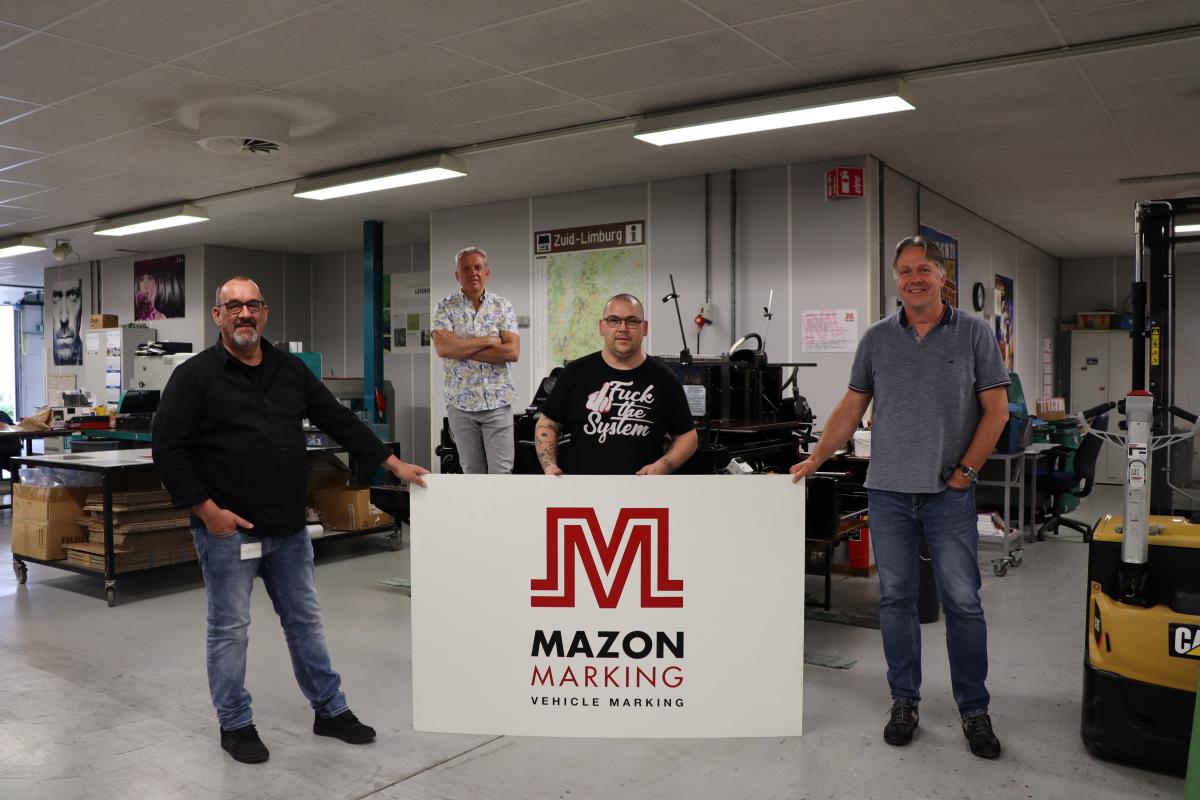 Tobias met jobcoach Albert, afdelingshoofd Paul en manager Alex achter logobord van Mazon