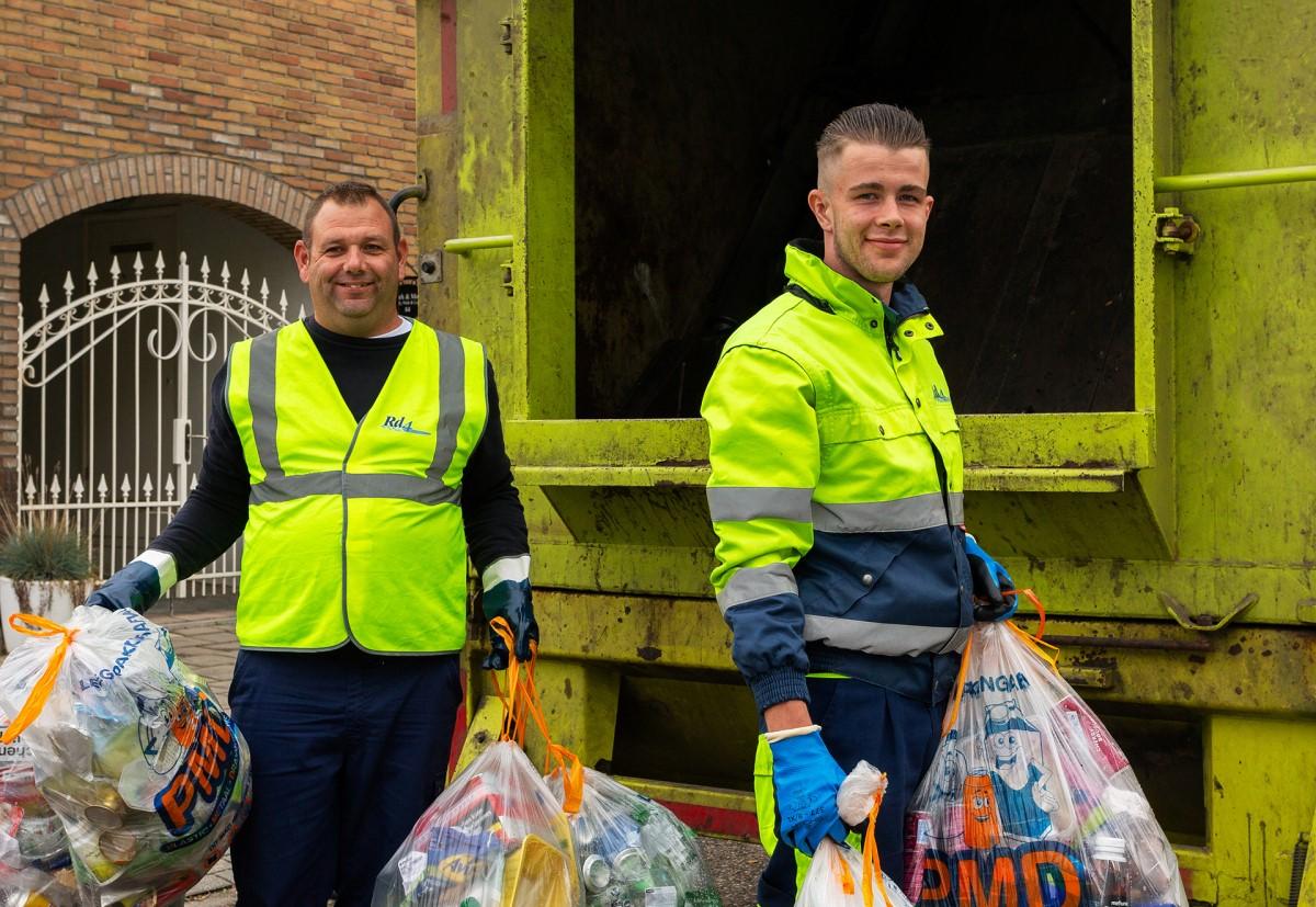 Twee afvalhelden met PMD zakken achter de vrachtwagen