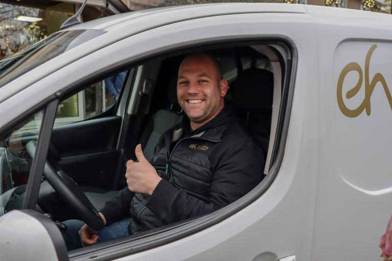 Wout met duim omhoog achter het stuur van bestelbus bloemist Ed Heuvelmans